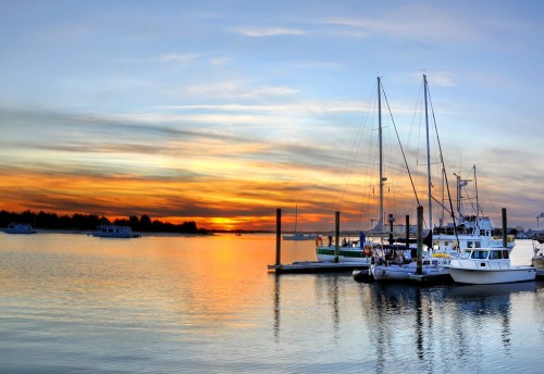 A serene marina at sunset, featuring boats docked and colorful skies reflecting on calm waters.