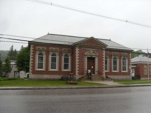 A brick building with large windows and a decorative entrance, set in a rainy landscape.