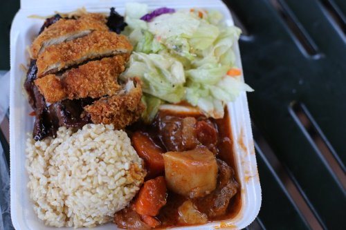 A takeout container with fried chicken, rice, salad, and a vegetable stew.
