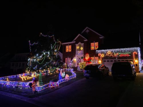 A festive house decorated with colorful Christmas lights, a large Santa, and a beautifully lit tree at night.