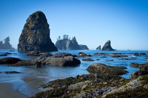Rocky coastline with towering sea stacks and calm blue waters under a clear sky.