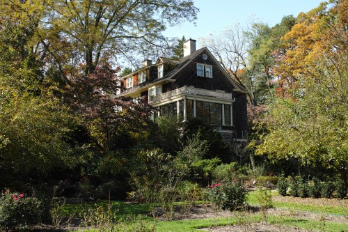 A large, elegant house surrounded by colorful trees and lush gardens in a serene outdoor setting.