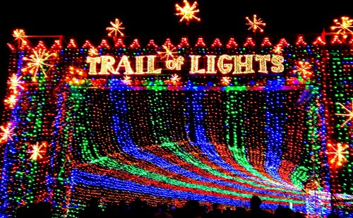 Colorful holiday lights create a vibrant display with the words "Trail of Lights" at the top.