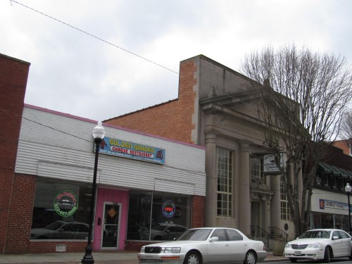 A street view of a small town featuring a restaurant with a colorful sign and a historic building next door.