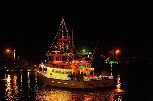 A brightly lit boat decorated with colorful lights and palm trees, floating on water at night.
