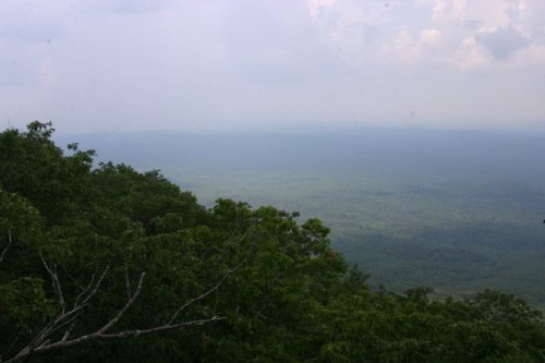 A panoramic view of a lush green landscape under a cloudy sky, with distant mountains fading into the horizon.