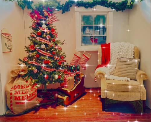 Cozy holiday scene with a decorated Christmas tree, stockings, and a chair, surrounded by festive decorations.