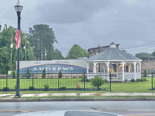 A gazebo in a park with a sign reading "Welcome to Historic Andrews" under a cloudy sky.