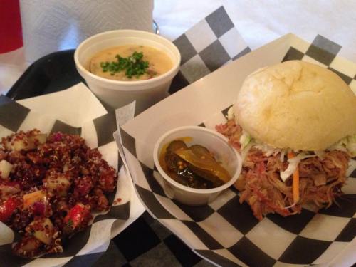 A plate featuring a pulled pork sandwich, a side of quinoa salad, and a cup of soup with green onions.