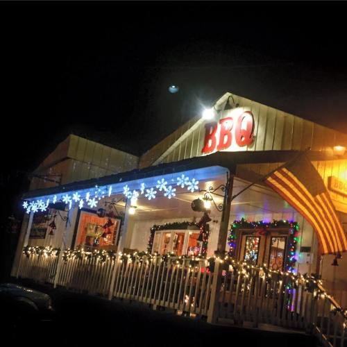 A cozy BBQ restaurant decorated with festive lights and an American flag, set against a night sky.