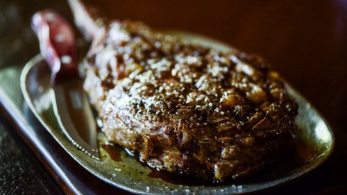 A beautifully cooked ribeye steak on a silver platter, garnished with salt and a red-handled knife beside it.