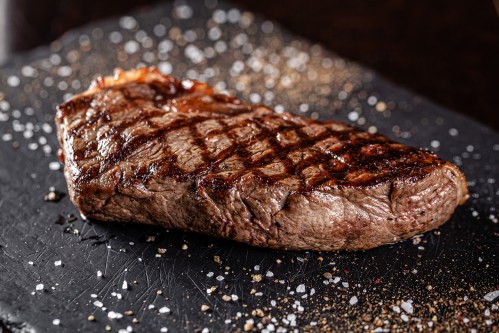 A perfectly grilled steak on a black slate plate, garnished with salt and pepper.