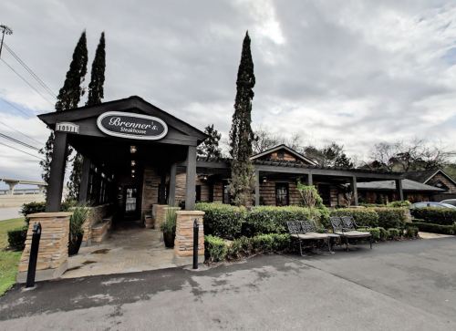 Exterior view of Brenner's Steakhouse, featuring a stone facade, greenery, and a cloudy sky.