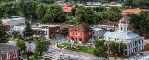 Aerial view of a small town featuring historic buildings, trees, and a train passing in the background.
