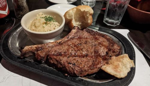 A sizzling steak on a platter with a side of mashed potatoes and a bread roll.