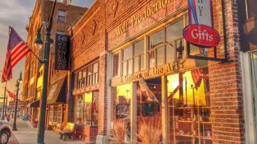 A vibrant street scene featuring a gallery and shops with warm sunset reflections on brick buildings.