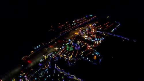 Aerial view of a vibrant display of colorful holiday lights illuminating a dark landscape.