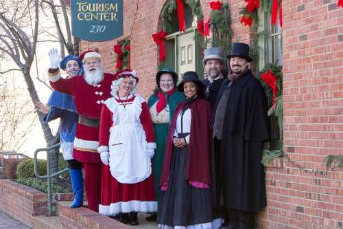 A festive group in Victorian costumes, including Santa, poses outside a tourism center decorated for the holidays.