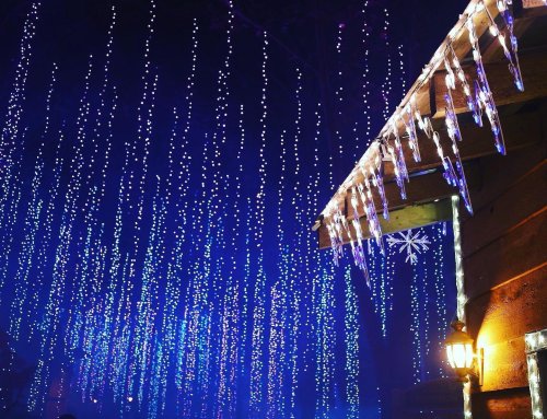 A cozy cabin adorned with blue and white icicle lights hanging from the roof, creating a festive winter atmosphere.