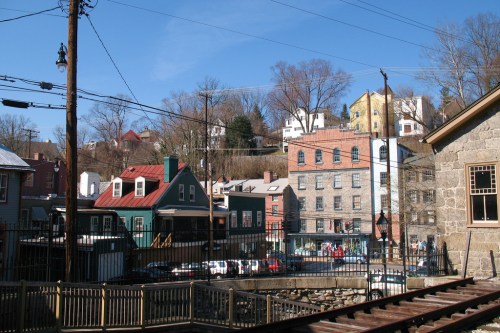 A view of colorful historic buildings on a hillside, with power lines and a railway in the foreground.