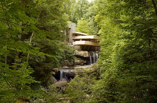 A modern house nestled in a lush green forest, with a waterfall cascading over rocks nearby.