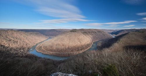 A panoramic view of a winding river surrounded by rolling hills and bare trees under a clear blue sky.