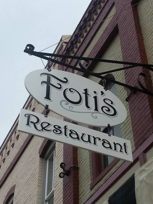 Sign for Foti's Restaurant hanging from a building, featuring a decorative design and bold lettering.