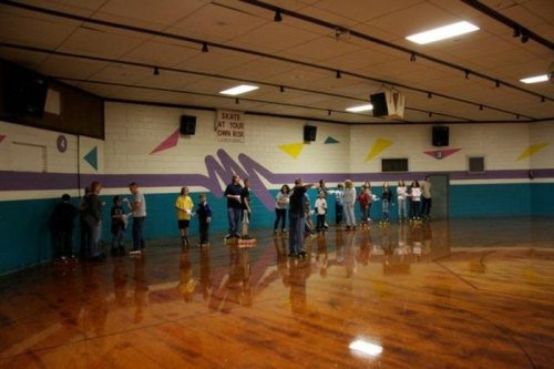 A group of people skating in a colorful roller rink with a shiny wooden floor and retro decor.