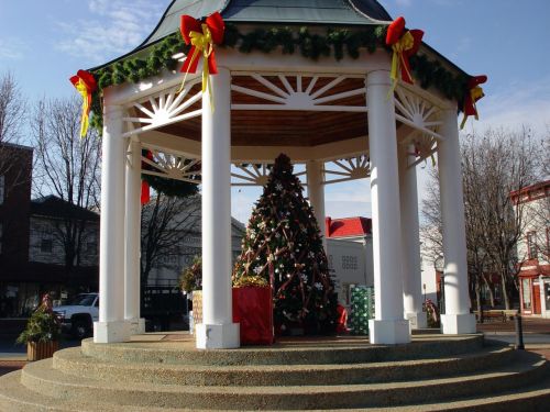 A decorated gazebo with a Christmas tree and presents, surrounded by festive garlands and ribbons.