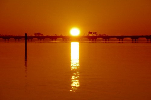 A golden sunset reflects on calm water, with a silhouette of a pier in the foreground.
