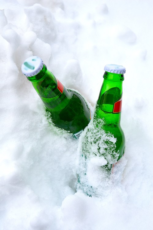 Two green glass bottles partially buried in white snow.