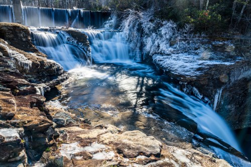 A serene waterfall cascades over rocky ledges, surrounded by icy formations and a tranquil pool below.