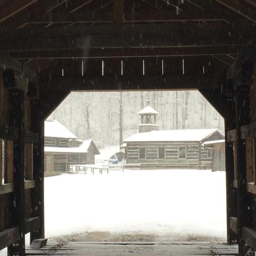 A snowy scene viewed through a wooden archway, with cabins and a tower in the background.