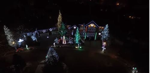 Aerial view of a house decorated with colorful Christmas lights and illuminated trees in a festive display.