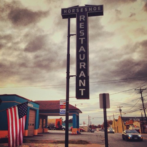 Sign for Horseshoe Restaurant with an American flag in front, set against a cloudy sky.