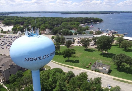 Aerial view of a blue water tower labeled "ARNOLD'S PARK" overlooking a lake and green park area.