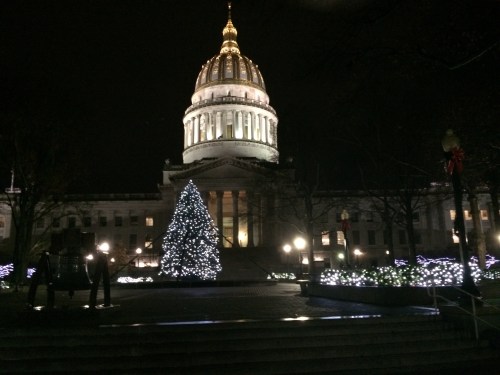 A lit Christmas tree in front of a grand capitol building at night, adorned with festive lights.