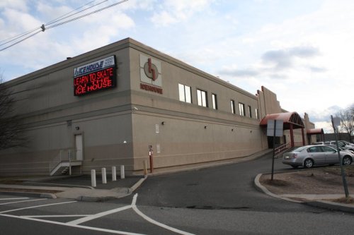 Exterior of an ice skating rink with a sign that reads "Learn to Skate" and a parking lot in front.