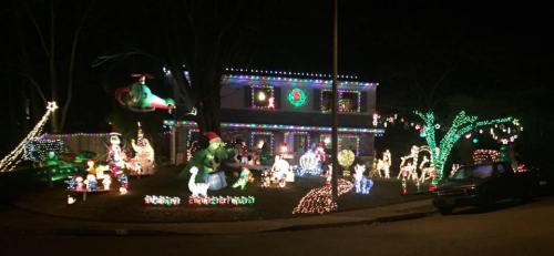 A house decorated with colorful Christmas lights, featuring various festive figures and a large wreath.