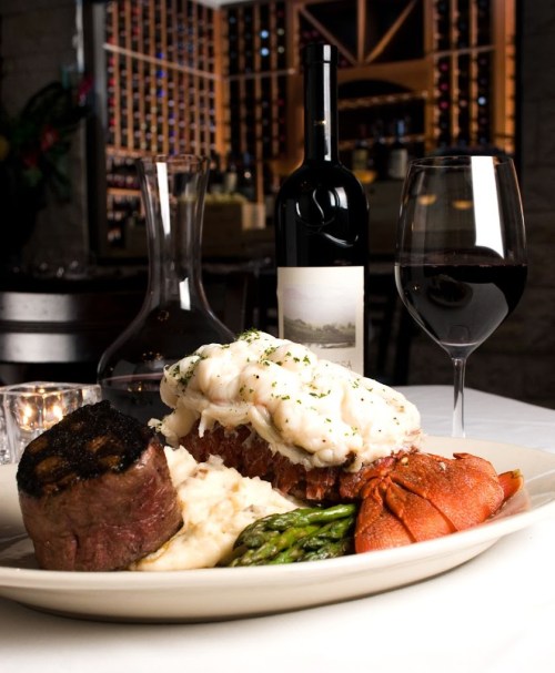 A gourmet plate featuring lobster, filet mignon, mashed potatoes, asparagus, and red wine in an elegant setting.