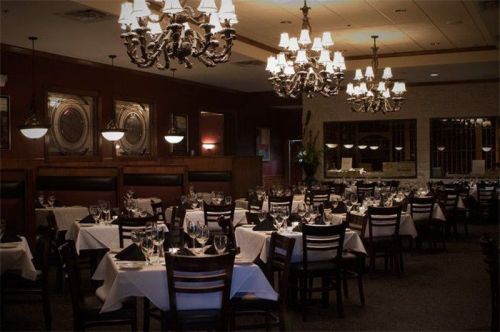 Elegant restaurant interior with chandeliers, white tablecloths, and neatly set tables. Warm, inviting atmosphere.