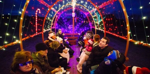 A festive scene of people sitting inside a brightly lit, decorated structure with colorful lights during the night.