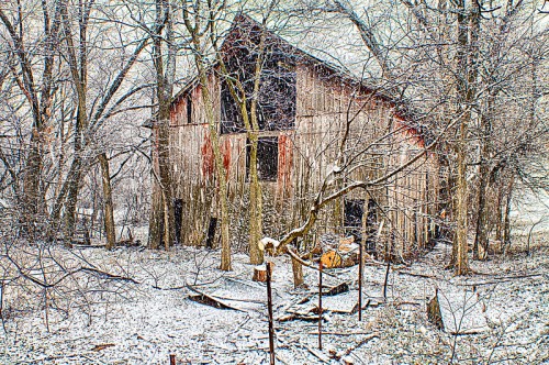 A weathered barn surrounded by snow-covered trees in a winter landscape.
