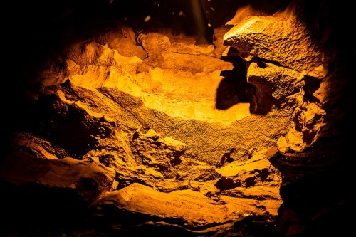A dimly lit cave interior with textured rock formations illuminated in warm orange tones.