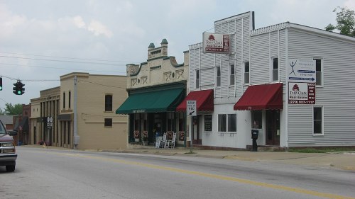 A small town street featuring historic buildings with awnings, shops, and a traffic light in the background.