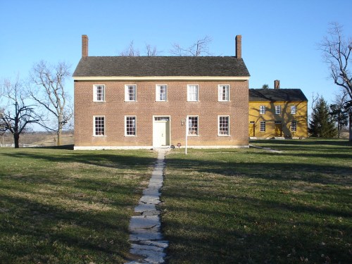 Two historic brick houses on a grassy landscape, with a stone path leading to the front door of the main house.