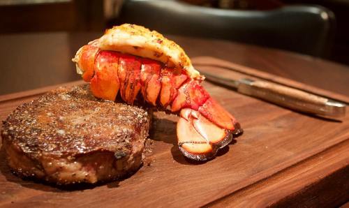 A beautifully plated steak with a lobster tail on top, served on a wooden board with a knife beside it.