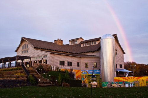 A rustic building with a silo, colorful murals, and a rainbow in the sky above.