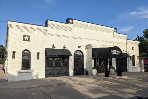 A white brick building with black awnings and star decorations, featuring large windows and a welcoming entrance.