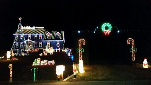 A brightly lit house decorated with colorful Christmas lights, featuring a tree, wreath, and festive figures in the yard.